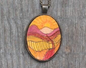 May include: A gold chain necklace with an oval pendant featuring a hand-painted landscape scene. The pendant depicts a sunset over rolling hills with a red path winding through the landscape.