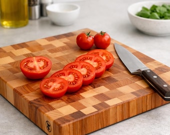 Puede incluir: Una tabla de cortar cuadrada de madera con un patrón de tablero de ajedrez en tonos marrón claro y oscuro. Sobre la tabla hay dos tomates cherry rojos enteros y cinco rodajas de tomate, junto a un cuchillo de cocina de acero inoxidable.