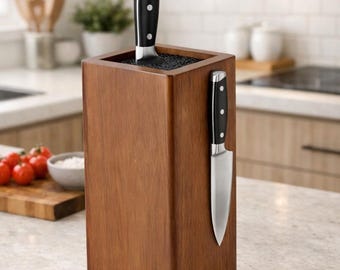 Puede incluir: Un bloque de madera rectangular para cuchillos con acabado marrón oscuro y base giratoria negra. El bloque cuenta con una ranura superior con cerdas negras para cuchillos y un panel lateral magnético que sostiene un cuchillo de acero inoxidable.