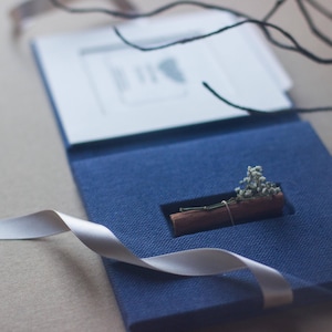 Peut inclure: Une boîte en lin bleu avec un ruban blanc et une petite cannelle avec des fleurs séchées à l'intérieur.