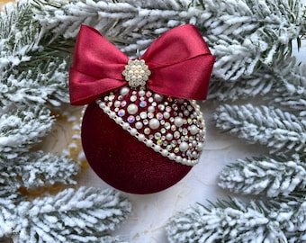 May include: A burgundy velvet Christmas ornament with a white pearl and rhinestone trim and a burgundy satin bow.