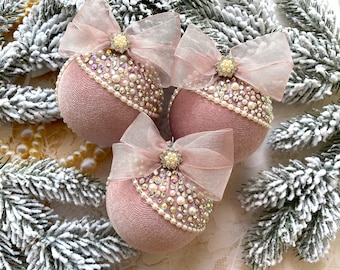 May include: Three blush pink velvet Christmas ornaments with a pearl and rhinestone trim and a sheer pink bow on each.