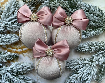 May include: Three blush pink velvet Christmas ornaments with gold trim and pearl accents. Each ornament has a large satin bow with a rhinestone and pearl embellishment.
