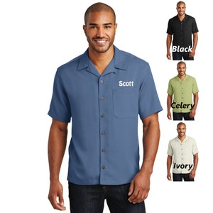 May include: A blue short-sleeved button-down shirt with a white collar and a pocket on the left side. The shirt has a name embroidered on the right side: "Scott".