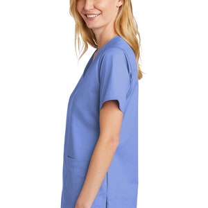 May include: A light blue scrub top with short sleeves and a v-neck. The top has a pocket on the left side and a small logo on the bottom right side.