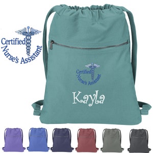 May include: Teal drawstring backpack with a zippered pocket and embroidered design of a medical caduceus with the text "Certified Nurse's Assistant" and the name "Kayla". The backpack is shown with other color options: purple, blue, navy, maroon, gray, and charcoal.