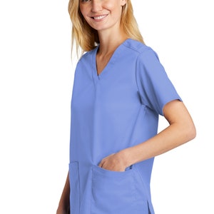 May include: A light blue medical scrub top with a V-neck and a single pocket on the left side. The scrub top has short sleeves and a side slit on the right side.
