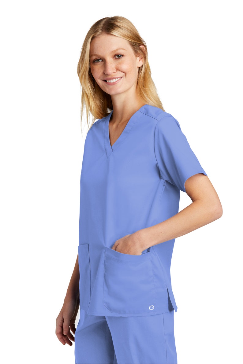 May include: A light blue medical scrub top with a V-neck and a single pocket on the left side. The scrub top has short sleeves and a side slit on the right side.