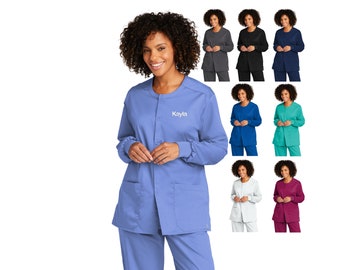 May include: A blue medical scrub top with long sleeves and a button-up front. The top has a round neckline and two pockets. The name "Kayla" is embroidered on the front of the top.