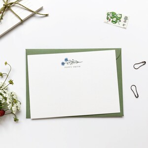 May include: A white card with a green envelope. The card has a blue floral design and the text "Poppy Smith" printed on it.