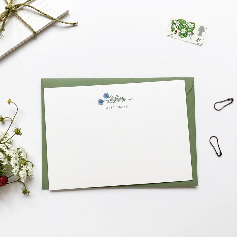May include: A white card with a green envelope. The card has a blue floral design and the text "Poppy Smith" printed on it.