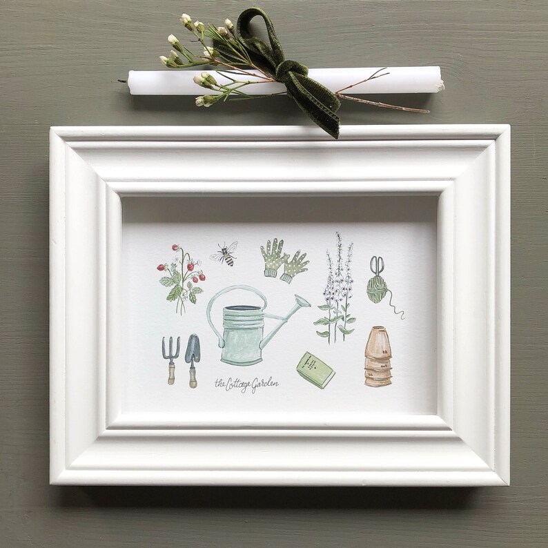 May include: A white framed print with a watercolor illustration of gardening tools and plants. The print says "The Cottage Garden" at the bottom.