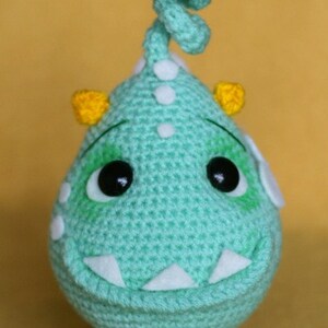 May include: A crocheted green monster with white eyes, yellow horns, and a white crocheted topknot. The monster has a white crocheted smile and white feet.