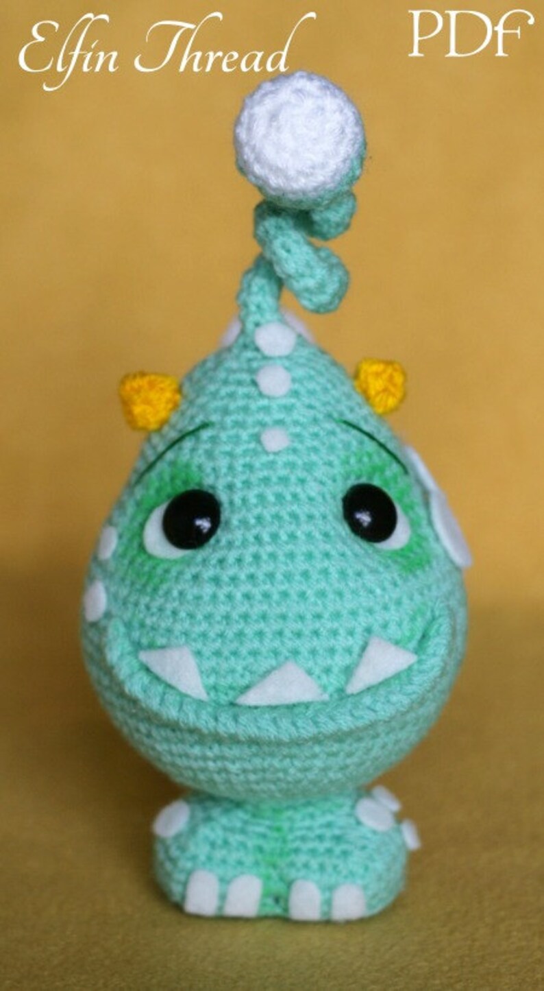 May include: A crocheted green monster with white eyes, yellow horns, and a white crocheted topknot. The monster has a white crocheted smile and white feet.