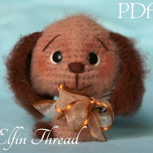 May include: A crocheted brown and white dog with brown ears and a gold and white bow. The dog is sitting on a blue surface. The text "Elfin Thread" is written below the dog. The text "PDF" is written in the upper right corner of the image.