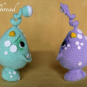 May include: Two crocheted amigurumi monsters, one green and one purple, with white spots and yellow accents. The monsters have long, curled tails and are standing on a beige surface. The text "Elfin Thread" is visible in the top left corner of the image, and "PDF" is visible in the top right corner.