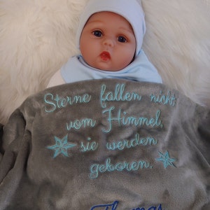 Könnte beinhalten: Eine graue Babydecke mit blauer Stickerei, die "Sterne fallen nicht vom Himmel, sie werden geboren." lautet. Die Decke trägt außerdem den Namen "Thomas Ferdinand" und das Datum "30.08.2022", ebenfalls in blau gestickt. Ein brauner Teddybär ist unten auf die Decke genäht.