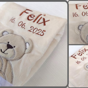 Puede incluir: Manta de bebé color crema con un aplique de oso de peluche y el nombre "Felix" bordado en marrón. La fecha "16. 06. 2025" también está bordada. Una cinta blanca está atada a la manta.