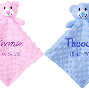May include: Two personalised baby blankets with attached plush bear heads. One blanket is pink with the name Leonie and the date 09.11.2020 embroidered on it. The other blanket is blue with the name Theodor and the date 12.10.2020 embroidered on it.