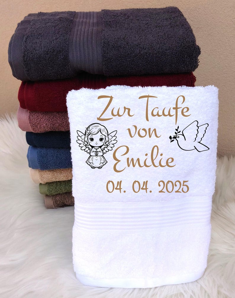May include: A stack of colorful bath towels, with a white towel in front. The white towel is personalized with the text "Zur Taufe von Emilie 04. 04. 2025", an angel illustration, and a dove illustration.