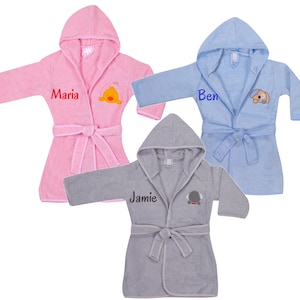 May include: Three hooded bathrobes in pink, blue, and gray with embroidered names and animal designs. The pink robe has the name "Maria" and a yellow duck, the blue robe has the name "Ben" and a brown dog, and the gray robe has the name "Jamie" and a gray elephant.