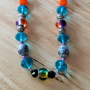 May include: A turquoise and orange beaded necklace with silver accents. The necklace features a variety of beads, including round, faceted, and patterned beads.
