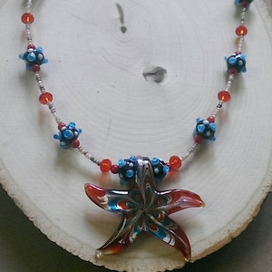 May include: A necklace with blue, red, and white glass beads and a starfish pendant. The starfish is made of glass and has a swirling pattern of red, orange, and blue.