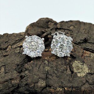 May include: A pair of silver stud earrings with a round halo of small diamonds.