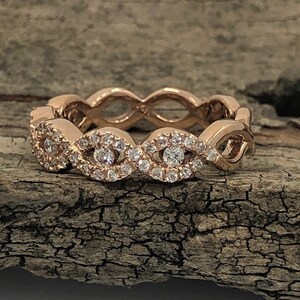 May include: A rose gold band ring with a delicate, intricate design featuring a row of small diamonds set in a wavy pattern.
