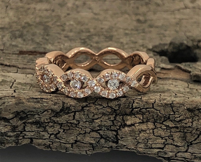 May include: A rose gold band ring with a delicate, intricate design featuring a row of small diamonds set in a wavy pattern.