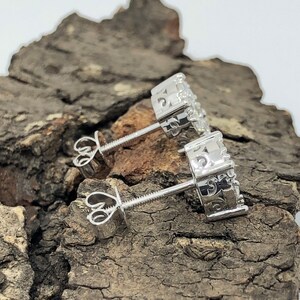 May include: A pair of silver stud earrings with a circular design and small clear stones. The earrings have a screw-back closure.