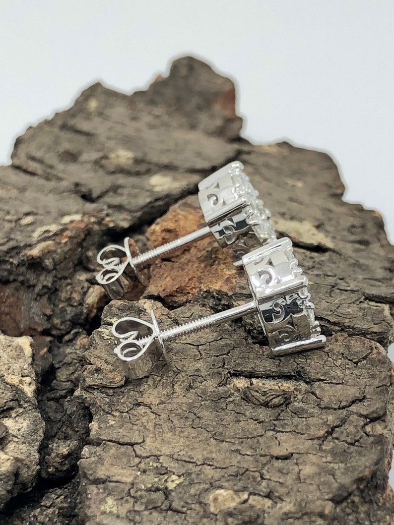 May include: A pair of silver stud earrings with a circular design and small clear stones. The earrings have a screw-back closure.