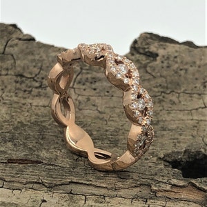 May include: A rose gold band ring with a delicate, intertwined design featuring small diamonds.