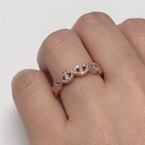 May include: A rose gold band ring with a delicate, wave-like design. The ring is set with small, clear cubic zirconia stones.