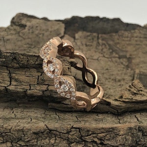 May include: A rose gold band ring with a delicate, interwoven design featuring small, clear diamonds.