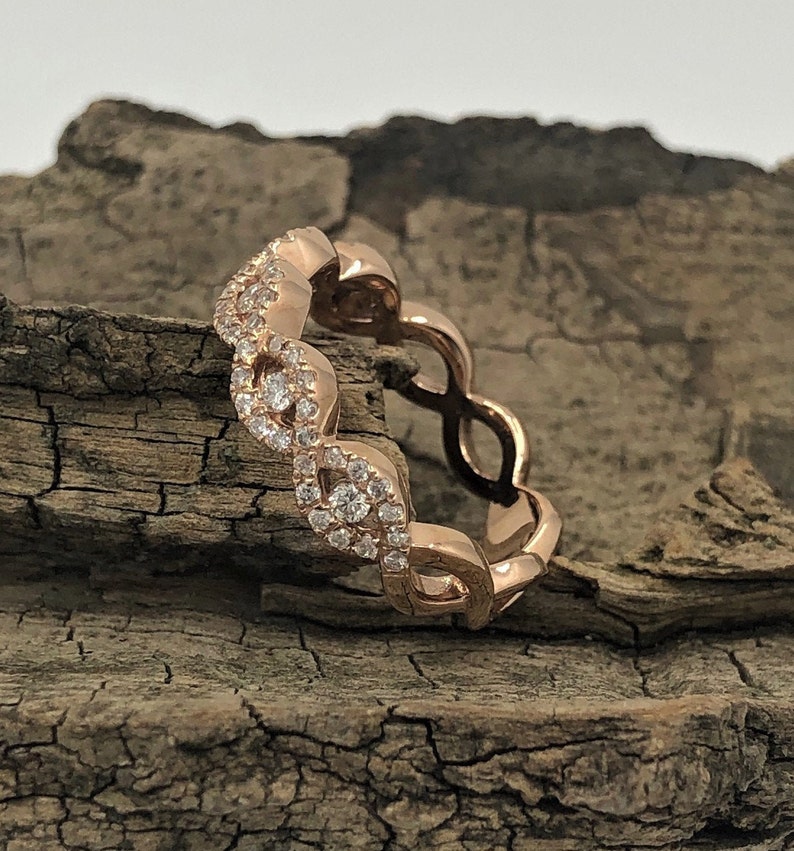 May include: A rose gold band ring with a delicate, interwoven design featuring small, clear diamonds.