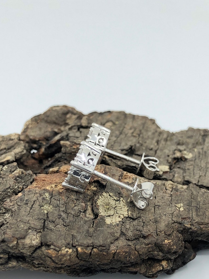 May include: A pair of silver earrings with a small, clear stone set in each earring. The earrings are on a wooden surface.