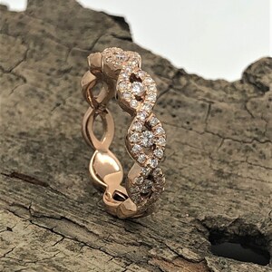May include: A rose gold band ring with a delicate, interwoven design. The band is set with small, sparkling diamonds.