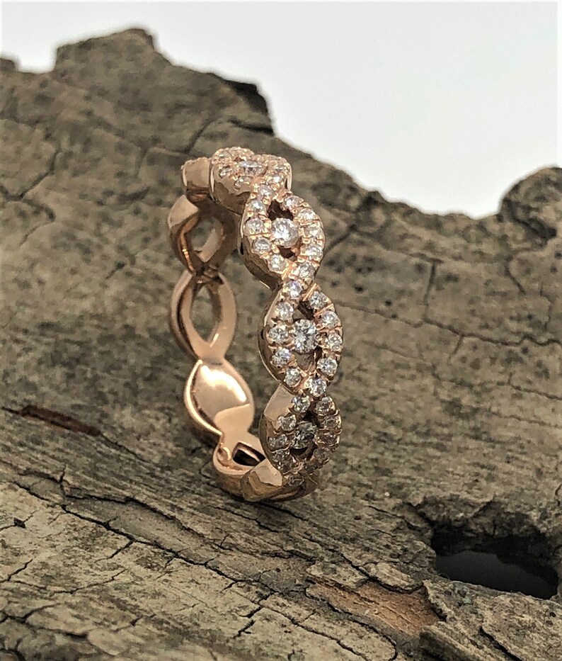May include: A rose gold band ring with a delicate, interwoven design. The band is set with small, sparkling diamonds.