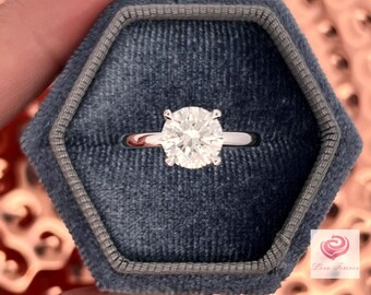 May include: A silver engagement ring with a large, round, clear diamond in a gray velvet ring box.