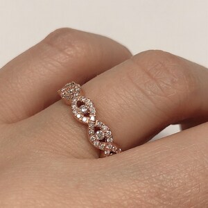 May include: A rose gold band ring with a delicate, intricate design featuring a series of connected oval shapes, each set with small diamonds.