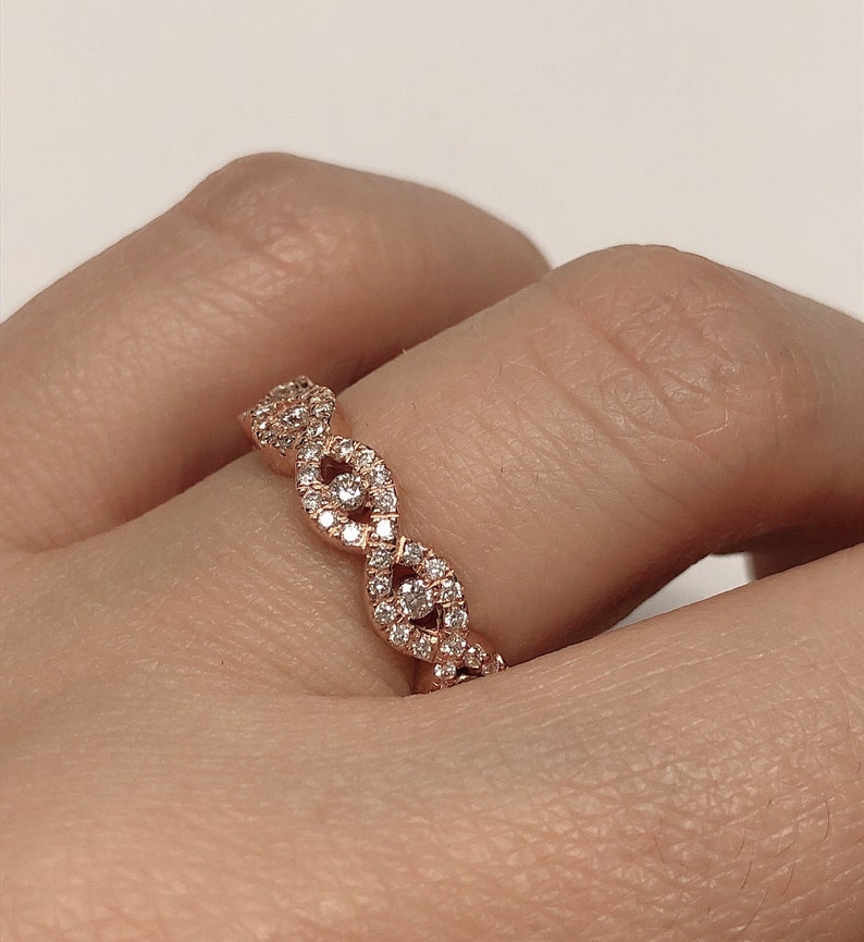 May include: A rose gold band ring with a delicate, intricate design featuring a series of connected oval shapes, each set with small diamonds.
