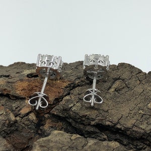 May include: A pair of silver stud earrings with a clear stone in the center. The earrings have a screw-back closure.