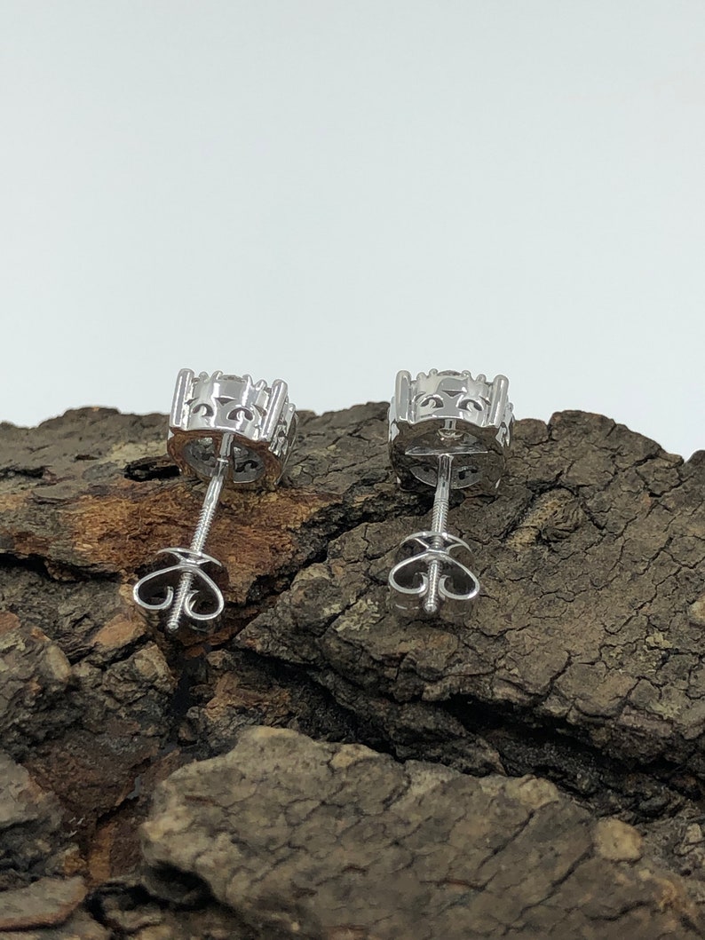 May include: A pair of silver stud earrings with a clear stone in the center. The earrings have a screw-back closure.
