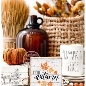 May include: A rustic autumn-themed display featuring a small wooden sign with "Hello Autumn" text and leaf graphics. A pumpkin, a mug with "Pumpkin Spice" text, and other fall decor are also present.