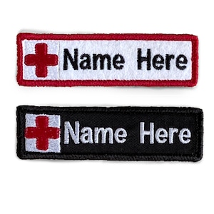 May include: Two embroidered patches with a red cross and the text "Name Here" in white. The top patch has a red border and a white background. The bottom patch has a black border and a black background.