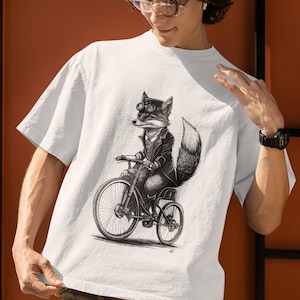 以下が含まれることがあります： 自転車に乗ったゴーグルをかけたキツネの白黒イラストが描かれた白いTシャツ