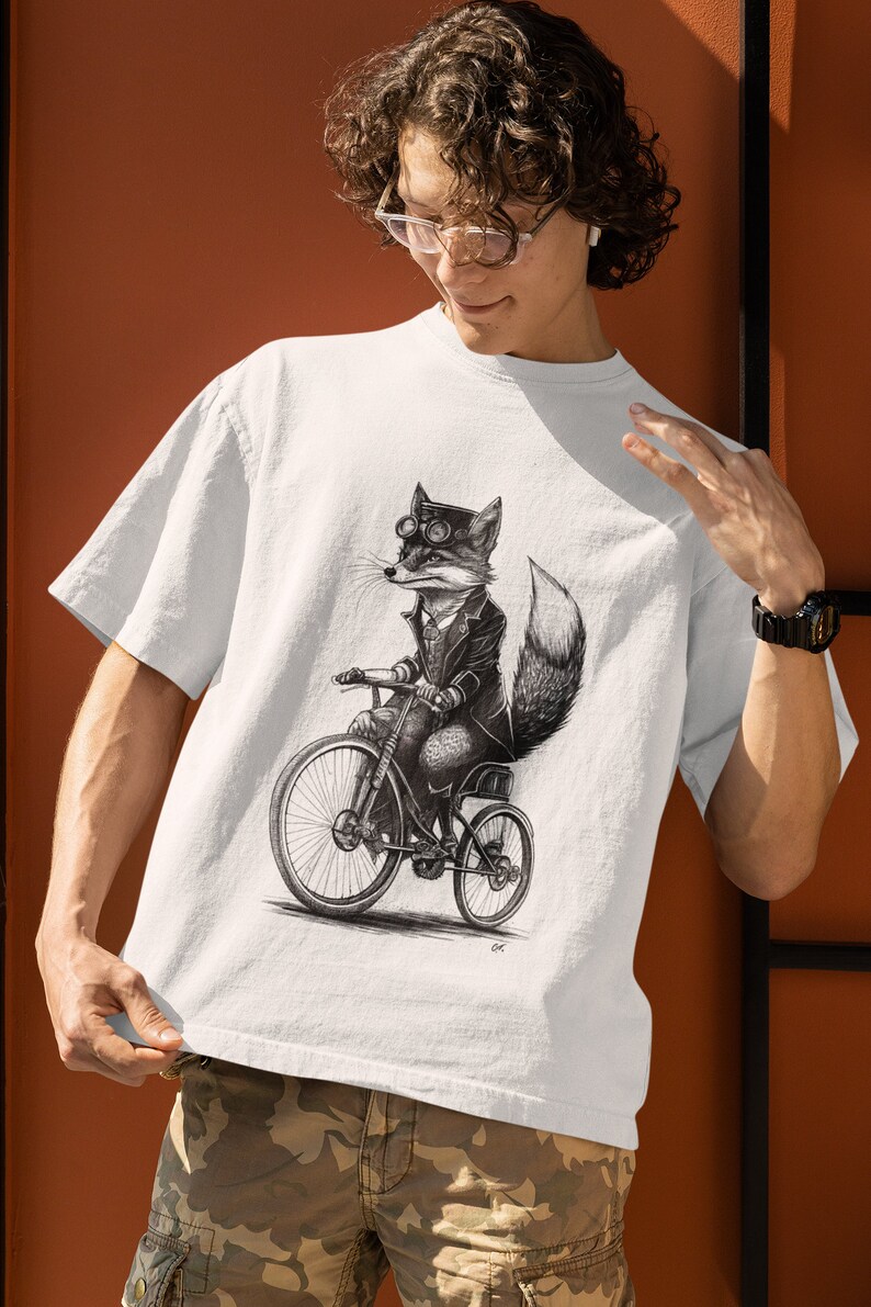 以下が含まれることがあります： 自転車に乗ったゴーグルをかけたキツネの白黒イラストが描かれた白いTシャツ