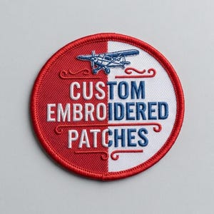 Pode incluir: Um emblema bordado circular com uma borda vermelha. O fundo é dividido verticalmente em metades vermelha e branca. Apresenta um ícone de avião azul no topo e o texto CUSTOM EMBROIDERED PATCHES em letras azuis e brancas.