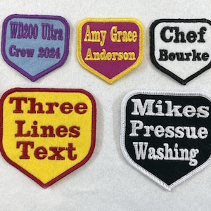 May include: Five embroidered patches with different text. The patches are shaped like a heart with rounded corners. The patches are in different colours: blue, purple, white, yellow, and black.